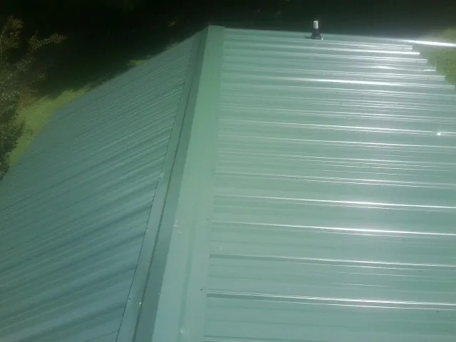 New green metal panels meeting at the ridge of a roof — Flat Roof Repair work by our crew in Prescott
