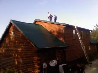 Crew on the ridge of a green metal roof on a two story log home in Prescott