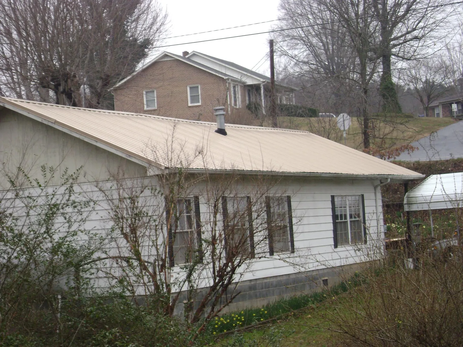 Tan metal roof on a white sided house set into a hillside — Commercial Roofing by Roofing Brothers in Prescott